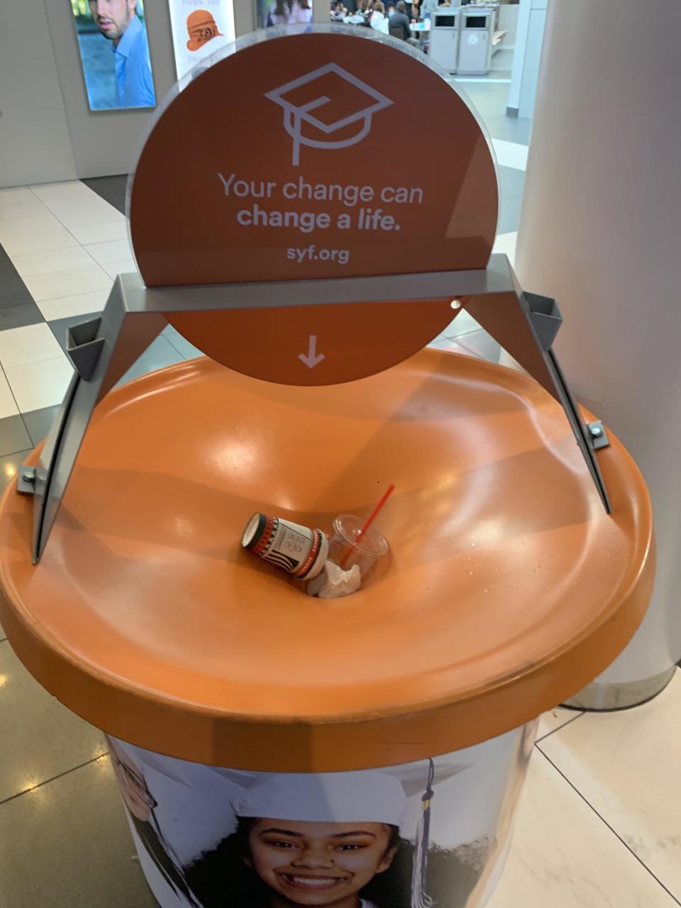 Donation station with a sign "Your change can change a life" with trash like a can, plastic cup, and straw on the collection surface