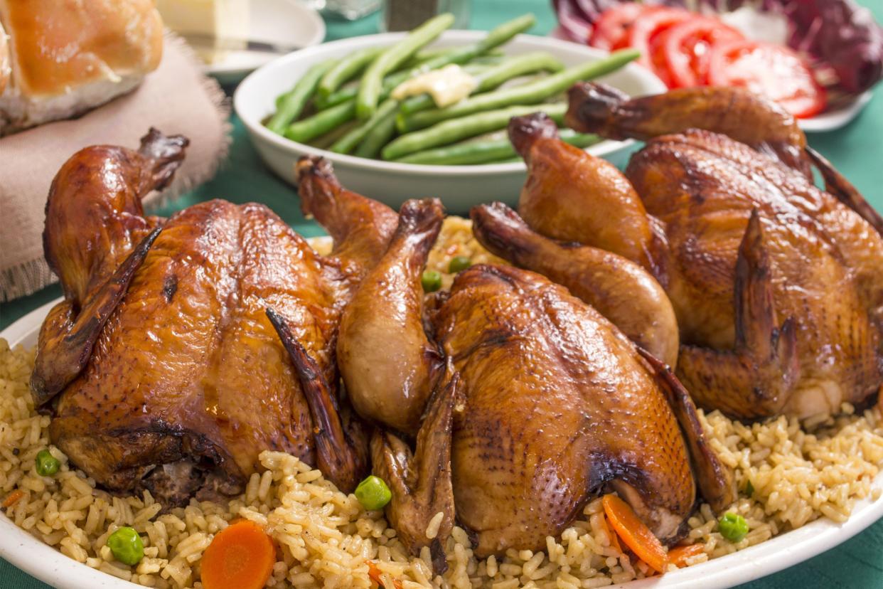 Three tender stuffed cornish hens on rice on a white plate with other festive foods in the background