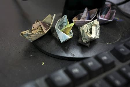 Venezuelan bolivar banknotes and a U.S. dollar banknote, folded as boats, are seen at a fruit and vegetable store in Caracas July 10, 2015. REUTERS/Marco Bello
