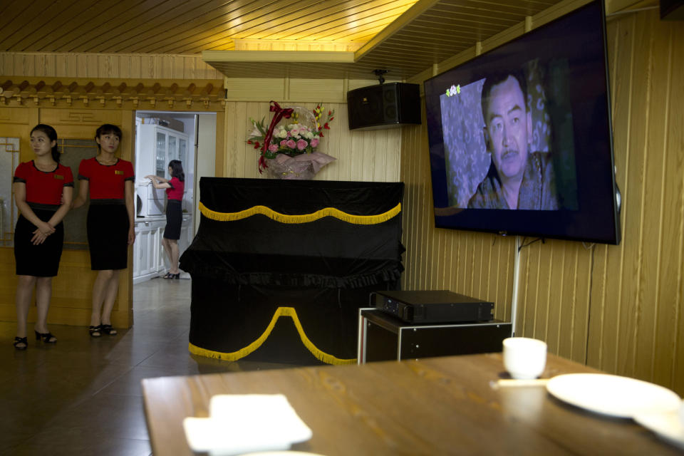 FILE - In this Wednesday, Aug. 15, 2018 photo, waitresses stand near a television screen showing a period drama in Pyongyang, North Korea. North Korean pop culture, long dismissed by critics as a kitschy throwback to the dark days of Stalinism, is getting a major upgrade under leader Kim Jong Un. The changes are being seen in everything from television dramas and animation programs to the variety and packaging of consumer goods, which have improved significantly under Kim. (AP Photo/Ng Han Guan, File)