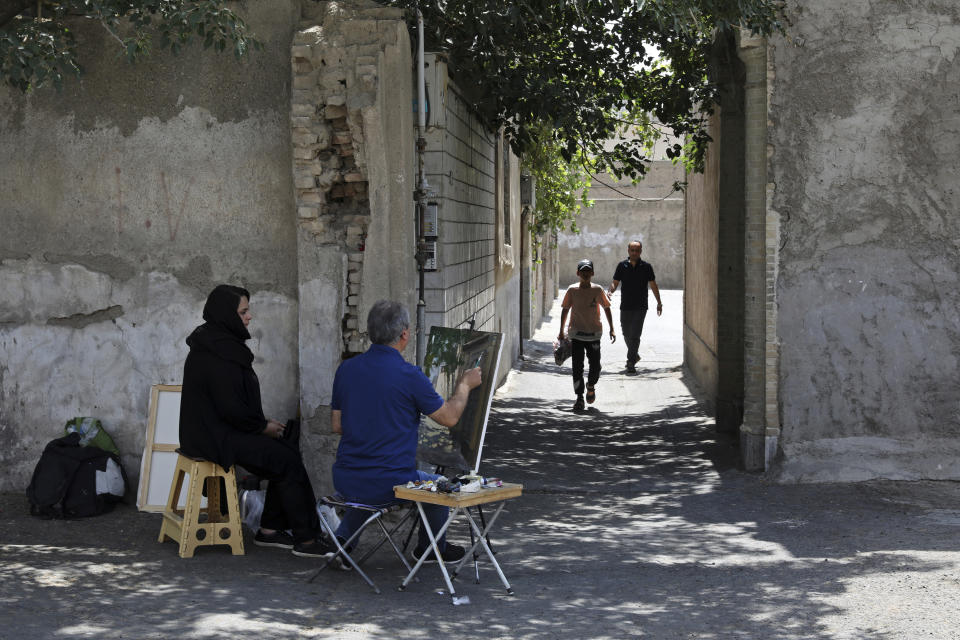 El pintor Hassan Naderali, junto a su asistente Minoo Amini, pinta un edificio antiguo en el barrio histórico de Oudlajan, en Teherán, Irán, el lunes 20 de junio de 2022. (Foto AP/Vahid Salemi)