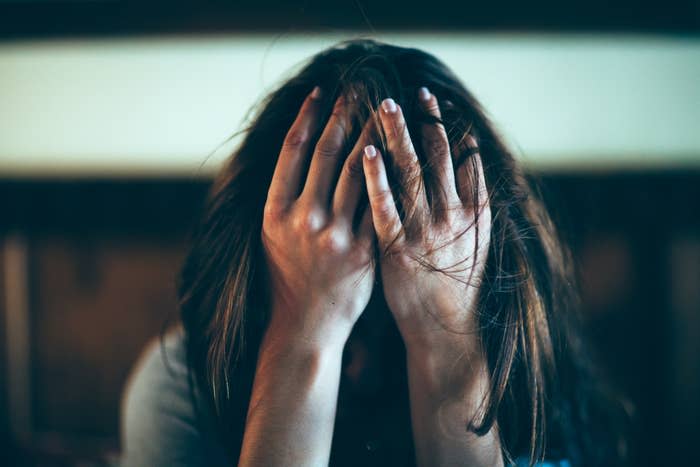 Person with long hair covering their face with their hands, seeming distressed