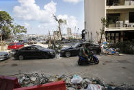 People ride past damaged cars in a neighborhood near the scene of Tuesday's explosion that hit the seaport of Beirut, Lebanon, Sunday, Aug. 9, 2020. Public fury over the massive explosion in Beirut took a new turn Saturday night as protesters stormed government institutions and clashed for hours with security forces, who responded with heavy volleys of tear gas and rubber bullets. (AP Photo/Thibault Camus)