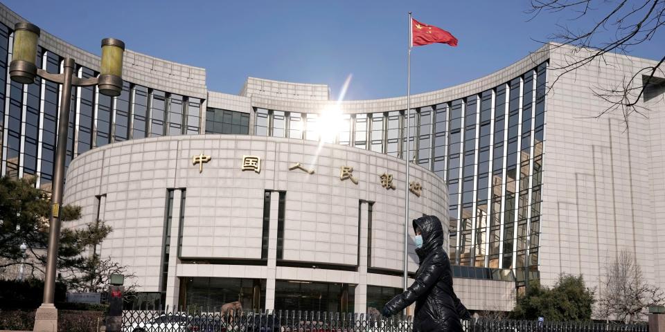 FILE PHOTO:  A woman wearing a mask walks past the headquarters of the People's Bank of China, the central bank, in Beijing, China, as the country is hit by an outbreak of the new coronavirus, February 3, 2020. REUTERS/Jason Lee/File Photo/File Photo