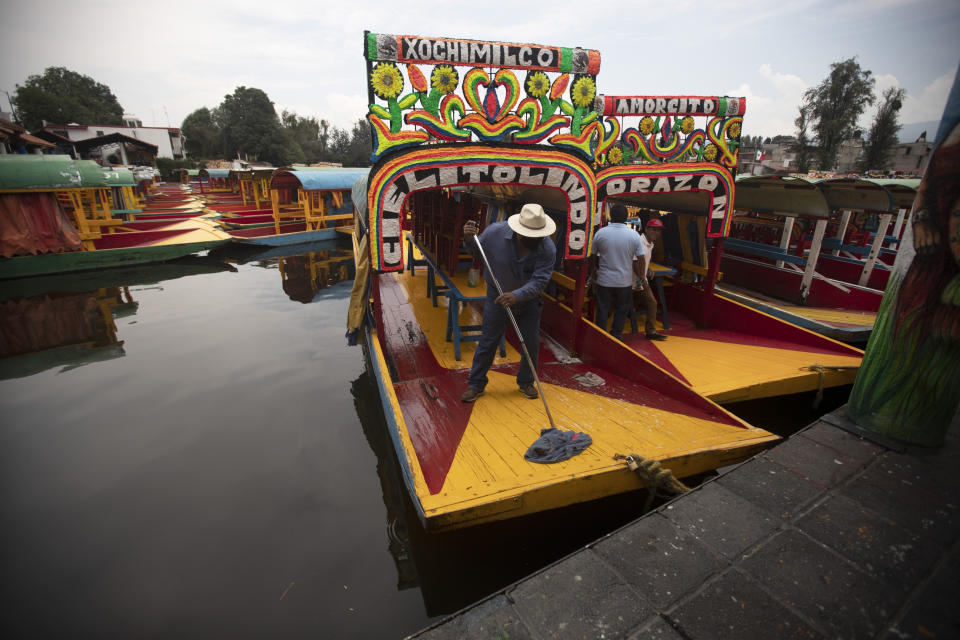 A man mops the deck of a painted wooden boat known as a trajinera, popular with tourists that ply the water canals in the Xochimilco district of Mexico City, during a reopening of activities after a six-month pause due to the COVID-19 pandemic. (AP Photo/Marco Ugarte)