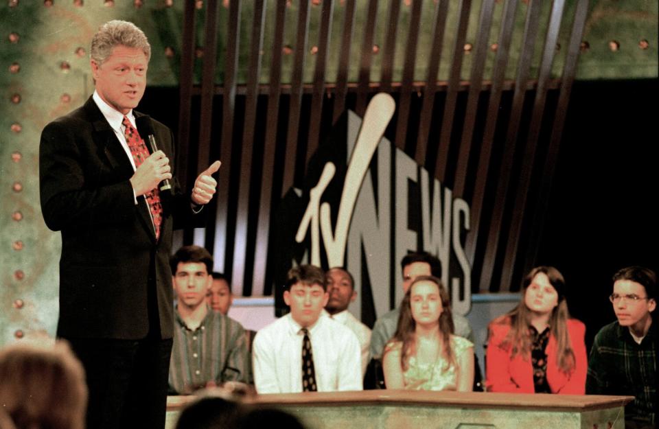 Bill Clinton holding a microphone with an audience behind him.