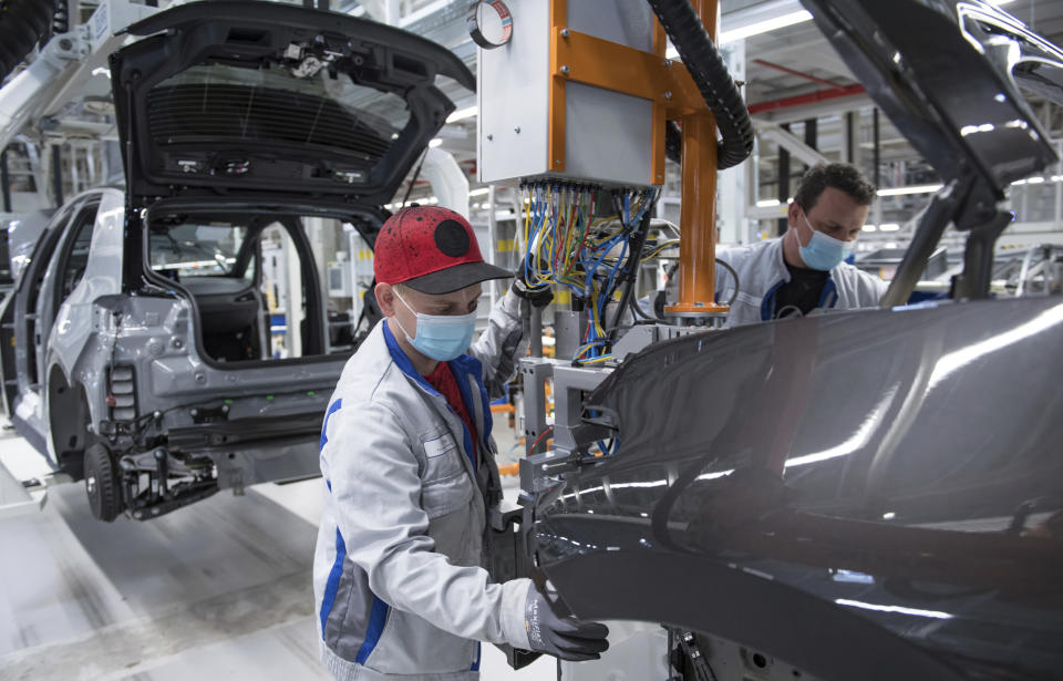 Sebastian Lohse, left, and Heiko Gruner employees of German car producer Volkswagen Sachsen, work with face masks in the assembly of the ID.3 in the vehicle plant in Zwickau, Germany, Thursday, April 23, 2020. At carmaker Volkswagen, vehicle production restarts after a corona shutdown of more than five weeks. Production of the all-electric ID.3 will initially be restarted with reduced capacity and cycle time. Zwickau is the first VW vehicle plant in Germany to resume operations. (Hendrik Schmidt/dpa via AP)
