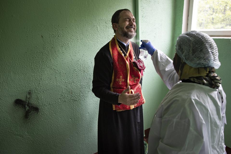 In this photo taken on Tuesday, May 26, 2020, a volunteer disinfects Father Vasily Gelevan after a visit to a patient suspected of being infected with COVID-19 at her apartment in Moscow, Russia. In addition to his regular duties as a Russian Orthodox priest, Father Vasily visits people infected with COVID-19 at their homes and hospitals. (AP Photo/Alexander Zemlianichenko)