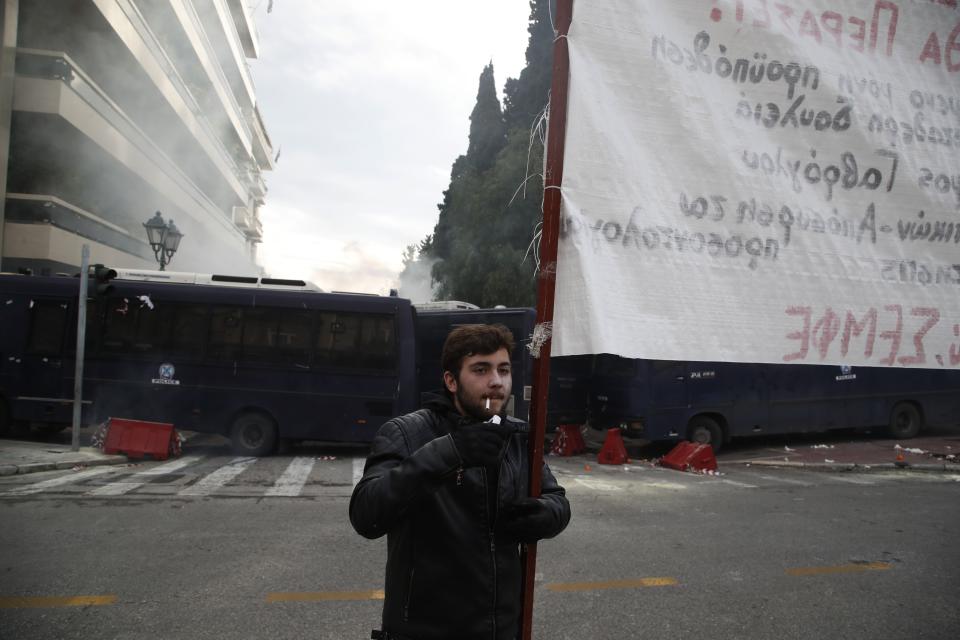 A protester smokes a cigarette after clashes near the Prime Minister's office in Athens, Friday, Jan. 11, 2019. About 1,500 people took part in the protest. Teachers' unions oppose the government's selection process for the planned hiring of 15,000 new teachers over the next three years. The banner reads ''Mass Full Time Hiring for Teachers.'' (AP Photo/Thanassis Stavrakis)