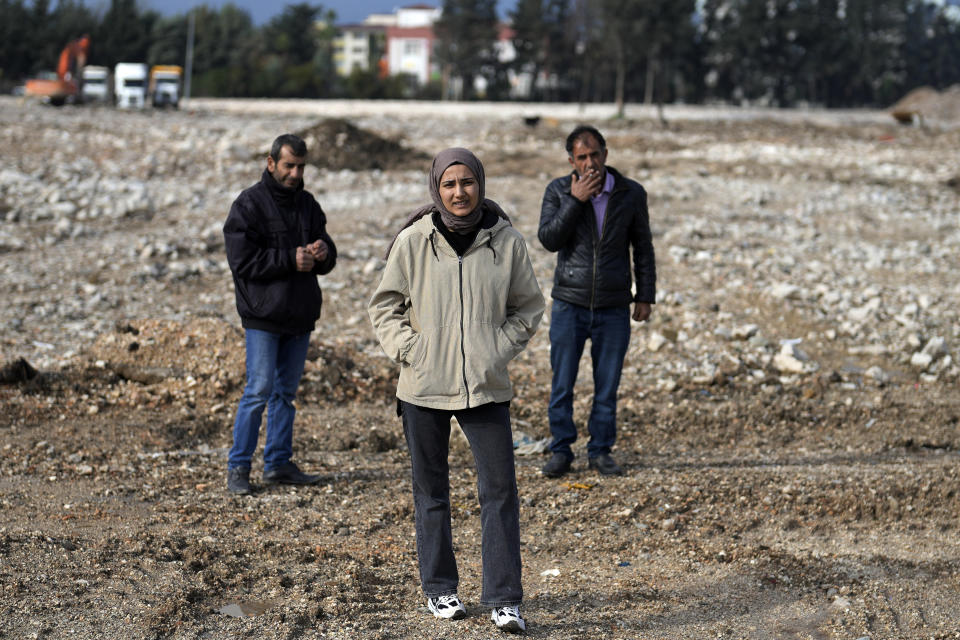 Sevda Kose, 22, center, stands on the ground where an eight-story apartment building that was home to her brother, his wife and their six-month old baby once stood in Antakya, southern Turkey, Thursday, Jan. 11, 2024. Kose’s relatives are still missing a year after the powerful Feb. 6, 2023 earthquake struck, reducing homes to rubble. (AP Photo/Khalil Hamra)