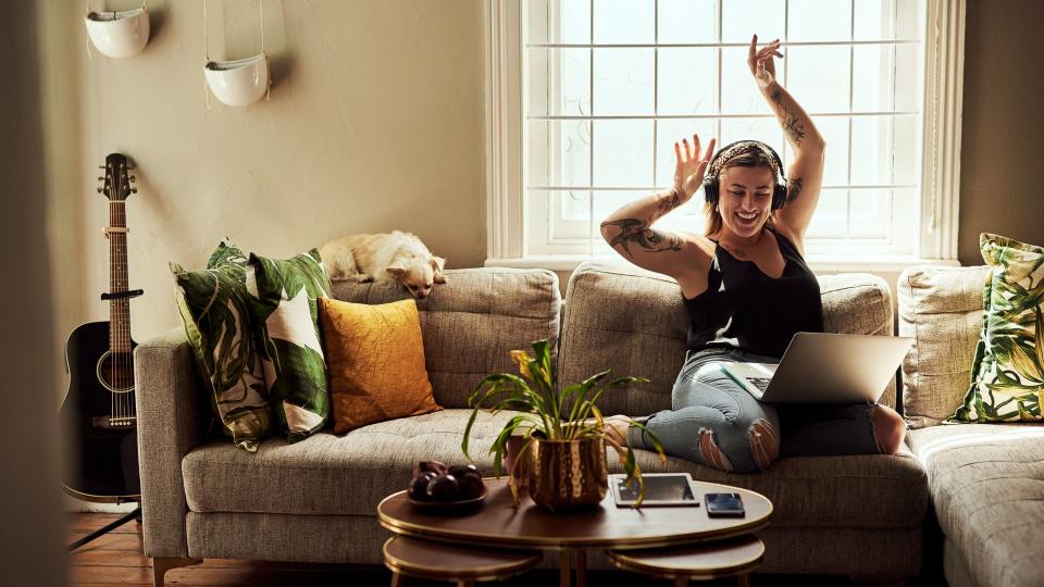 Shot of a young woman using a laptop and headphones on the sofa at home.