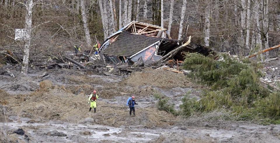 Searchers walk near a demolished house following a deadly mudslide that happened several days earlier, Tuesday, March 25, 2014, in Arlington, Wash. At least 14 people were killed in the 1-square-mile slide that hit in a rural area about 55 miles northeast of Seattle on Saturday. Several people also were critically injured, and homes were destroyed .(AP Photo/Elaine Thompson)