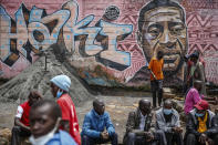 Local residents sit next to a mural painted in June 2020 showing George Floyd with the Swahili word "Haki" or "Justice" in the Kibera low-income neighborhood of Nairobi, Kenya, Wednesday, April 21, 2021. After three weeks of testimony, the trial of the former police officer charged with killing George Floyd ended swiftly: barely over a day of jury deliberations, then just minutes for the verdicts to be read — guilty, guilty and guilty — and Derek Chauvin was handcuffed and taken away to prison. The guilty verdict in the George Floyd trial was not just America's victory. It signaled hope for those seeking racial justice and fighting police brutality across the Atlantic. (AP Photo/Brian Inganga)