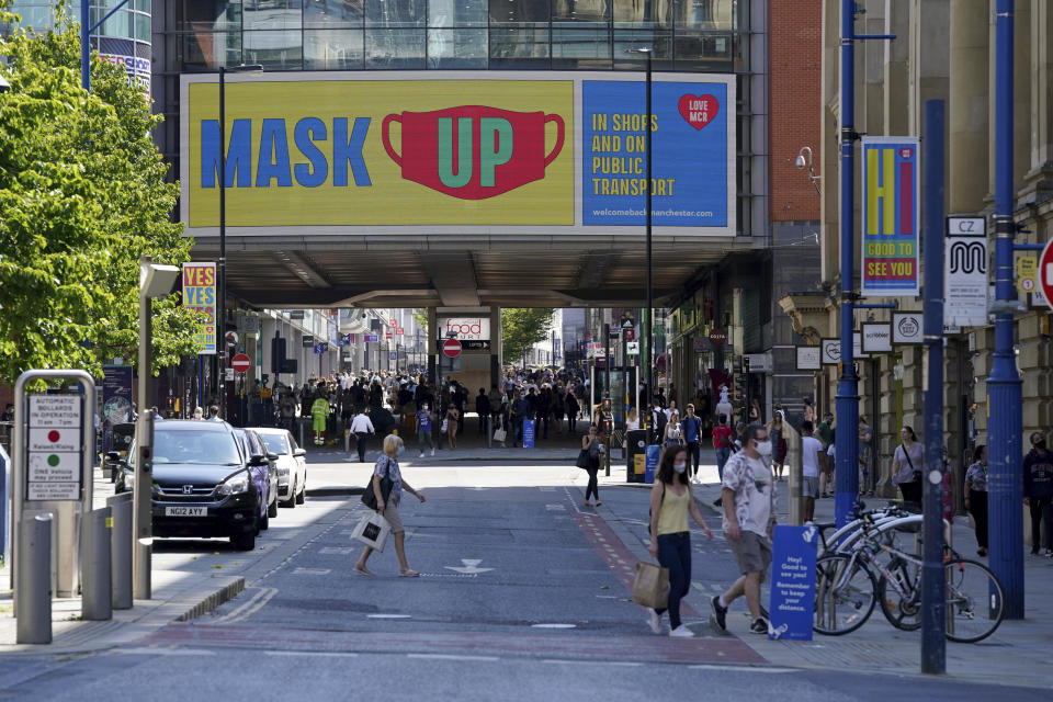 People wearing face masks to try to stop the spread of coronavirus walk backdropped by a "Mask Up" sign in Manchester, northern England, Friday, July 31, 2020. The British government on Thursday night announced new rules on gatherings in some parts of Northern England, including Manchester, that people there should not mix with other households in private homes or gardens in response to an increase trend in the number of cases of coronavirus cases per 100,000 people. (AP Photo/Jon Super)