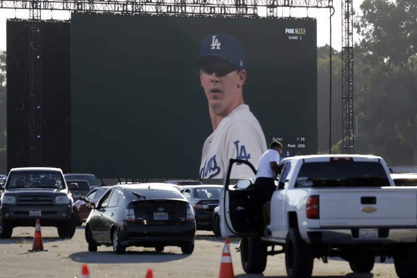 LOS ANGELES, CA - OCTOBER 12: Dodger pitcher Walker Buehler is broadcast on a screen as a fan cleans off his windshield to see through the late afternoon glare during a drive-in viewing party on Monday, Oct. 12, 2020 in Los Angeles, CA for the National League Championship Series against the Atlanta Braves in Arlington, Texas. (Myung J. Chun / Los Angeles Times)