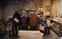 Wearing masks to curb the spread of the new coronavirus, the Delgado family poses for a photo in their carpentry workshop in El Alto, Bolivia, Friday, Aug. 28, 2020. After the government canceled the school year, the five children between ages 6 and 14 work in the carpentry workshop with their parents. (AP Photo/Juan Karita)