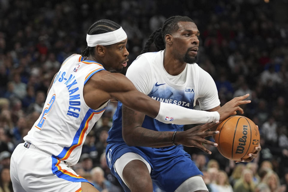 Minnesota Timberwolves center Naz Reid, right, handles the basketball as Oklahoma City Thunder guard Shai Gilgeous-Alexander (2) defends during the first half of an NBA basketball game, Saturday, Jan. 20, 2024, in Minneapolis. (AP Photo/Abbie Parr)