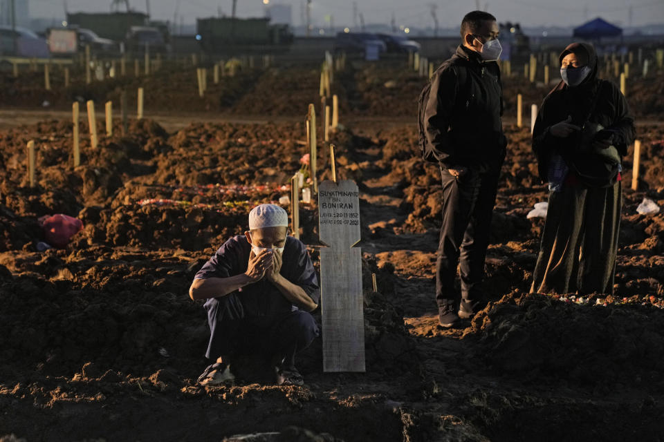 A man prays at the grave of a relative who died of COVID-19 during a burial at Rorotan Cemetery in Jakarta, Indonesia, Thursday, July 1, 2021. New land around the capital city continues to be cleared for the dead and gravediggers have to work late shifts following surges in COVID-19 cases fueled by travel during the Eid holiday in May, and the spread of the delta variant of the coronavirus first found in India. (AP Photo/Dita Alangkara)