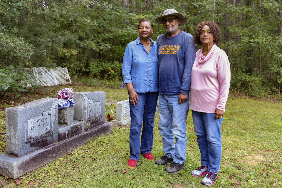 This Oct. 4, 2021 photo provided by the Mississippi Center for Justice, siblings Florine Robbins Stewart, left, Henry Robbins and Gwendolyn Robbins Pratt stand by their parents' gravesite on family land in Winston County, Miss. They and their relatives are receiving legal help from Mississippi Center for Justice to hold onto the land. The center providing aid to low-income families in more than half of Mississippi counties with heirs' property, which is passed down without a will and becomes owned in common by multiple family members. Such land can lack proper legal documentation, making it vulnerable to being taken over by others or lost when property taxes are not paid on time. (Patrick Taylor/Mississippi Center for Justice via the AP)