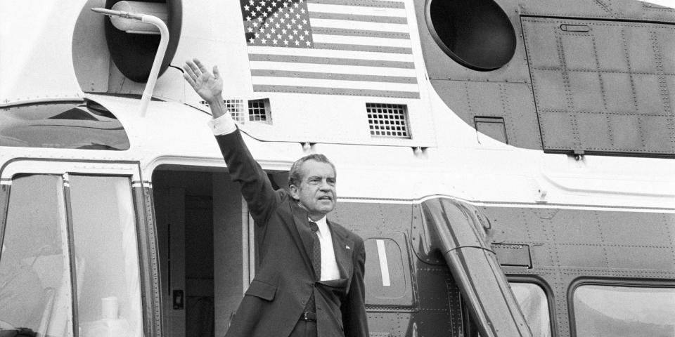 A black and white photo of Richard Nixon waving in front of a helicopter.