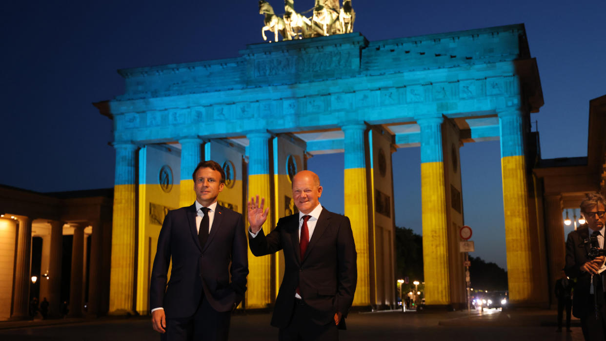  French President Emmanuel Macron and German Chancellor Olaf Scholz stand in front of the Brandenburg Gate. 