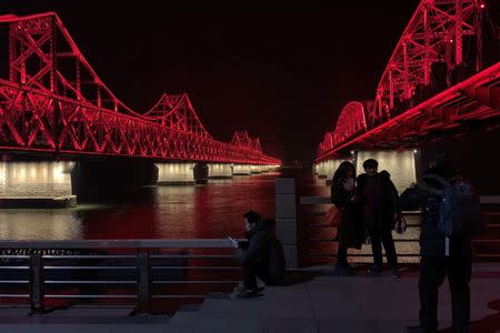 Visitors pose for pictures near the Friendship Bridge (L), which leads to North Korea's Sinuiju across the Yalu River, before a train believed to be carrying North Korean leader Kim Jong Un travels to China through the bridge, in Dandong, Liaoning province, China February 23, 2019. REUTERS/Tingshu Wang