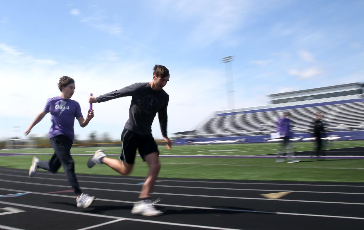 Jackson Burnes, left, hands a baton to Brady Cannon, right, at Liberty's track and field in North Liberty, Iowa ahead of the Drake Relays.