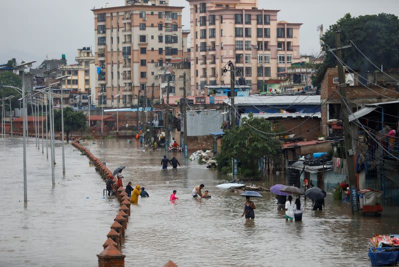 People walk along a flooded road along the bank of overflowing Bagmati river following heavy rains, in Kathmandu
