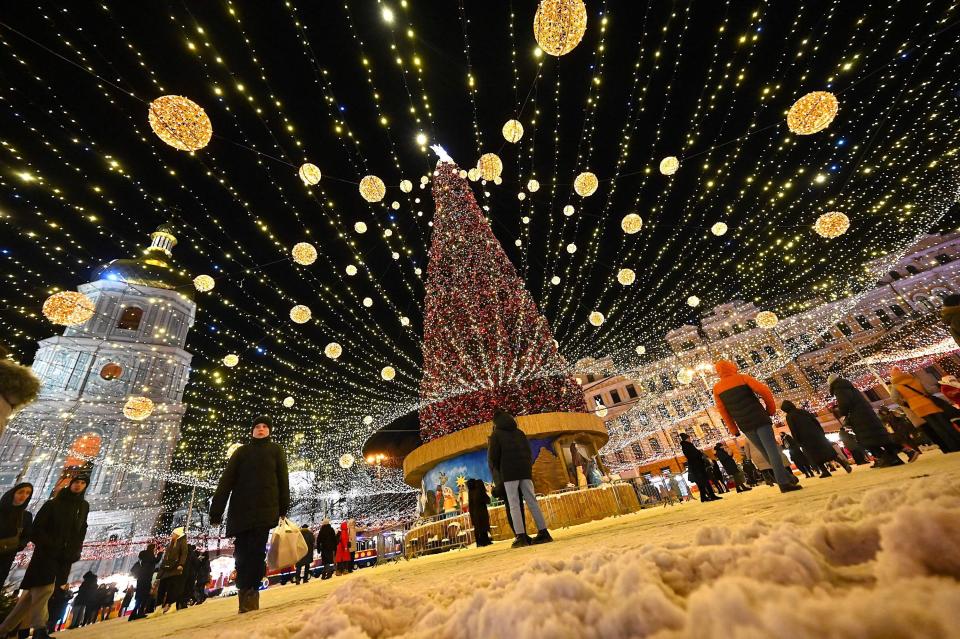 christmas tree and lights in a square filled with snow as people bundled up walk through kyiv