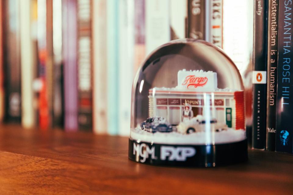 A snow globe with little cars and a diner that says "Fargo" on top sitting on a bookshelf.