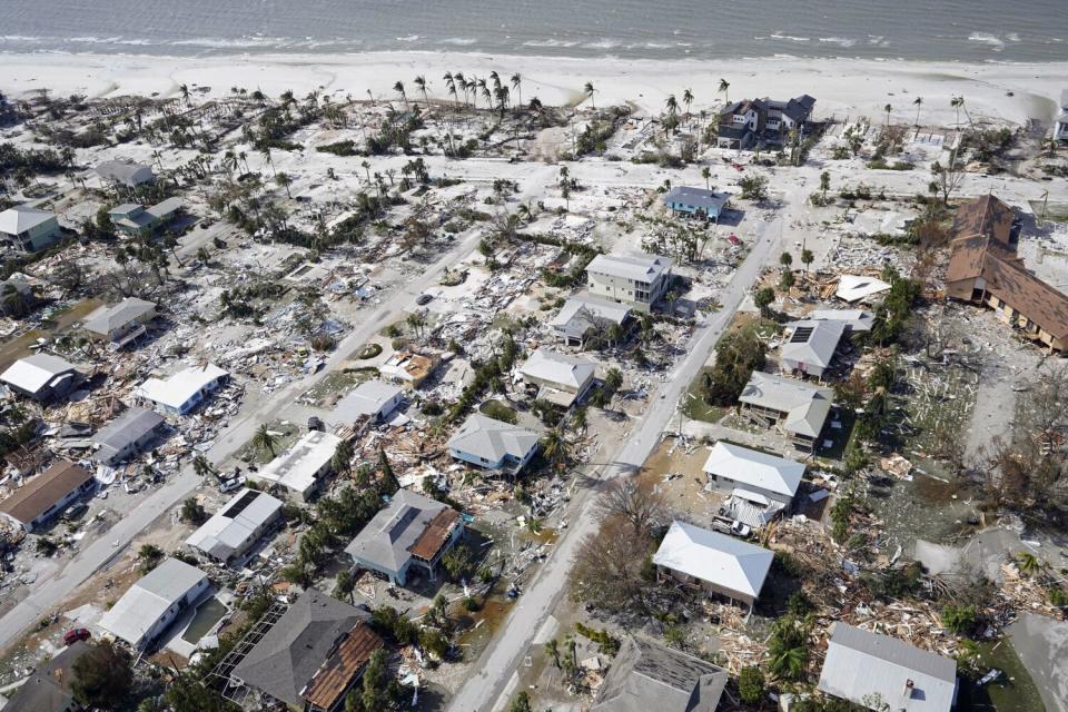 A beach-side neighborhood with many destroyed or damaged homes and debris.