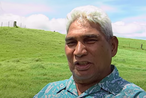 Close-up of a man with a grassy hill behind him