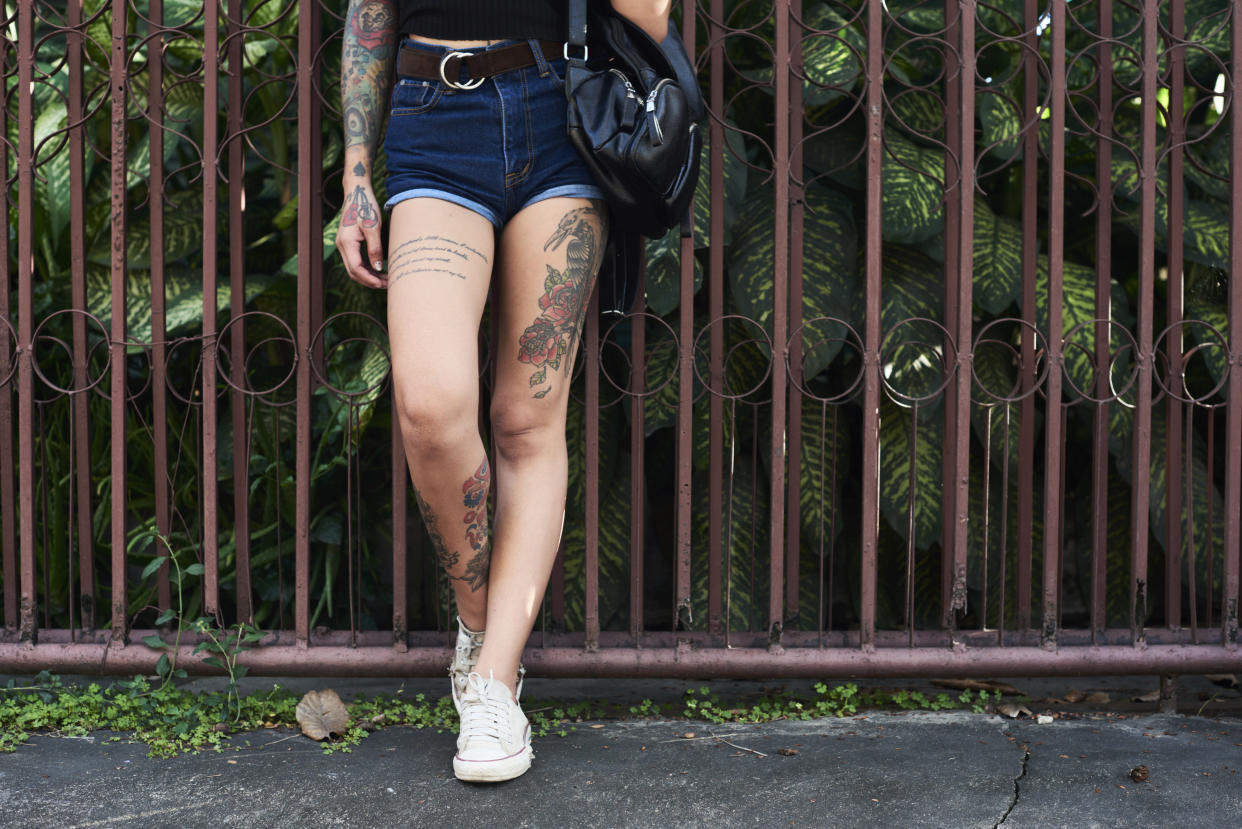 Legs of tattooed woman standing at garden fence