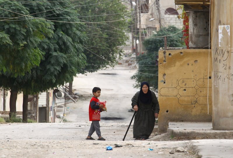 An elderly woman and a child are seen along a deserted street in the town of Ras al-Ain