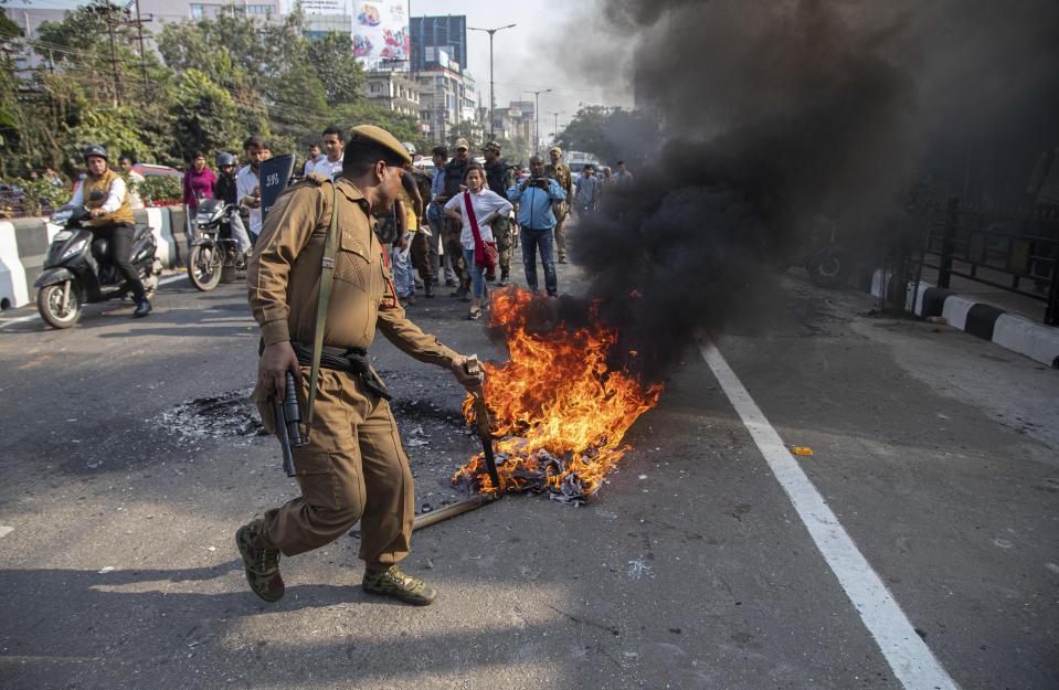 A policeman tries to douse a fire set by protestors against the Citizenship Amendment Bill (CAB) in Gauhati, India, Wednesday, Dec. 11, 2019. Protesters burned tires and blocked highways and rail tracks in India's remote northeast for a second day Wednesday as the upper house of Parliament began debating legislation that would grant citizenship to persecuted Hindus and other religious minorities from Pakistan, Bangladesh and Afghanistan. (AP Photo/Anupam Nath)