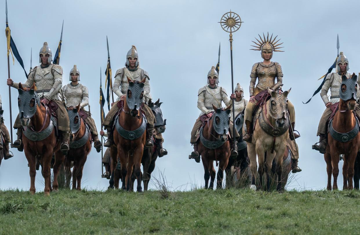 Actors dressed in what appear to be armored costumes are atop horses and lined up in a grassy area.