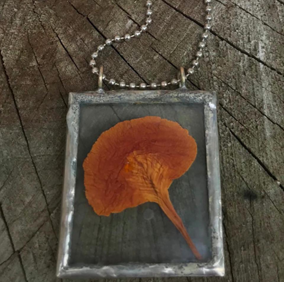 A pressed Royal Poinciana bloom retains some of its brilliance in this pendant by Liz Juneau, made of recycled glass, unleaded silver solder, collected and found objects on an 18-inch silver ball chain.