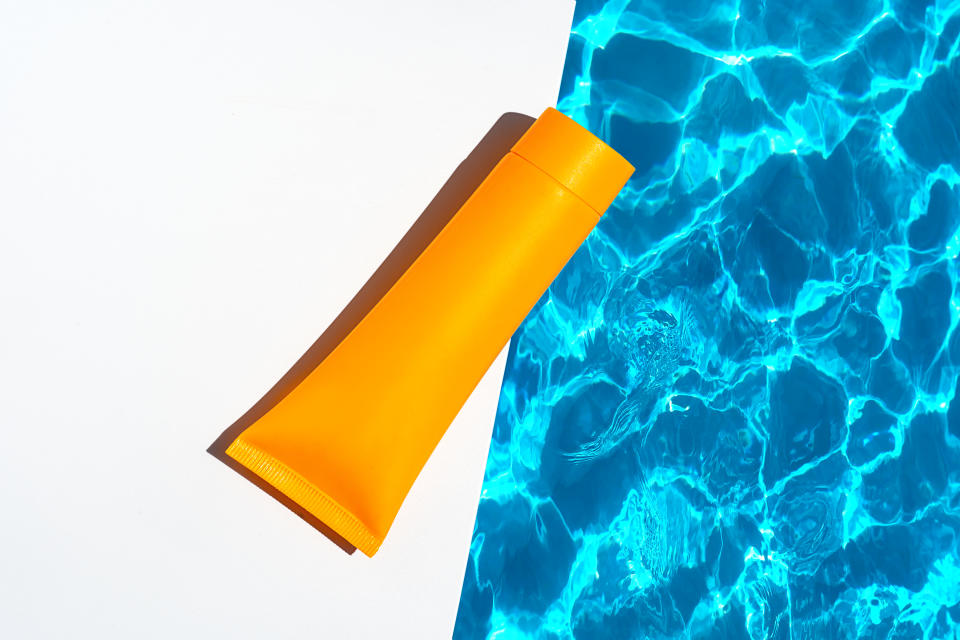 Orange tube with suntan lotion, cosmetic face cream or hand cream, shower gel, shampoo against the background of blue turquoise water with waves from the swimming pool.  Body, Hair Skin care nature concept.  Flat lay. Copy space. Close-up.