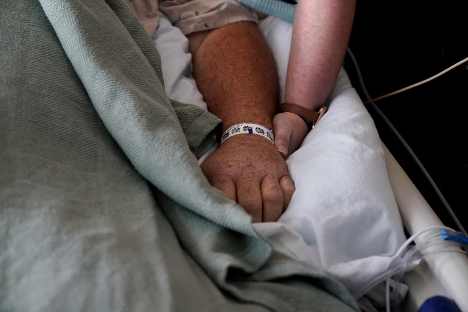 Lauren Debroeck, who is on oxygen as she recovers from COVID-19, holds the hand of her husband, Michael, as she talks to him, as he is kept alive with the help of an oxygenation machine, at the Willis-Knighton Medical Center in Shreveport, La., Wednesday, Aug. 18, 2021. Both contracted the virus, and Lauren is recovering. (AP Photo/Gerald Herbert)