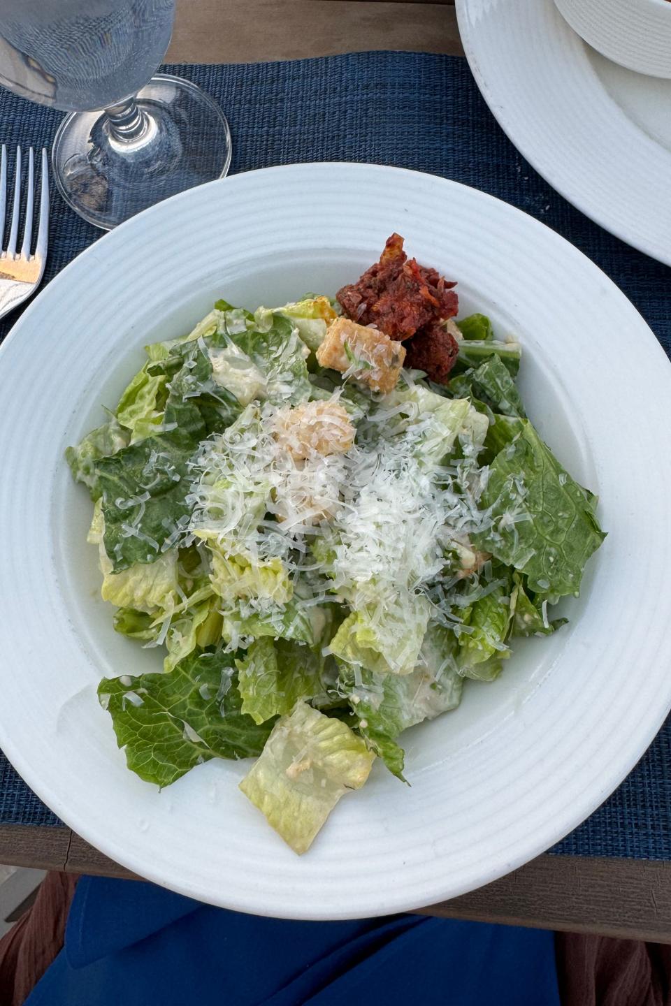 A Caesar salad with shredded cheese and croutons on a plate, at an outdoor dining setting