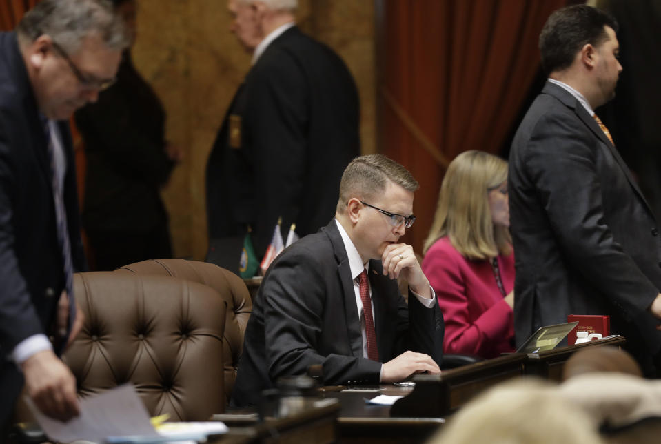 Washington State Rep. Matt Shea, R-Spokane Valley, center, reads at his desk on the floor of the House, Monday, April 22, 2019, at the Capitol in Olympia, Wash., as others leave the floor for a caucus meeting. Gov. Jay Inslee and other Democrats in Washington state are a criticizing Shea for appearing to support spying on political opponents, after The Guardian newspaper reported Saturday it had obtained the contents of messaging chats involving Shea and three other men discussing the topic. (AP Photo/Ted S. Warren)