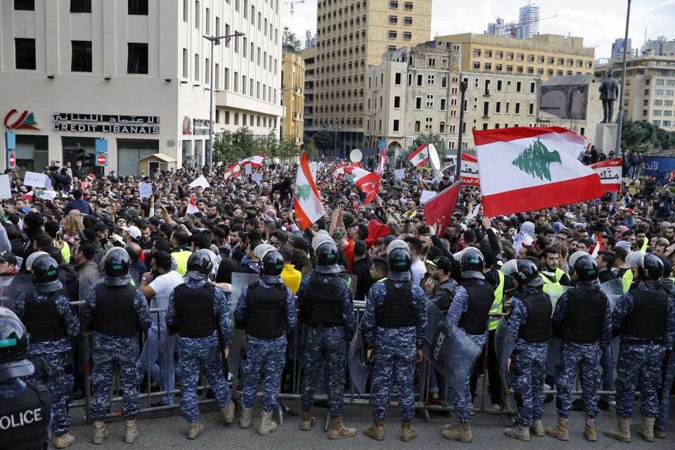 Anti-government protesters hold Lebanese flags and chant slogans as riot police stand guard in front of the government building, in central Beirut, Lebanon, Sunday, Dec. 23, 2018. Hundreds of Lebanese protested against deteriorating economic conditions as politicians are deadlocked over forming a new government. (AP Photo/Bilal Hussein)