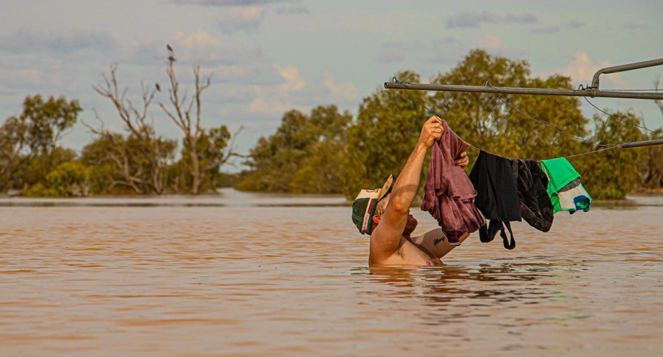 An Aussie hanging out washing in chest high floodwater while wearing a cap with four items of clothing on the line in Birdsville, central Queensland. 