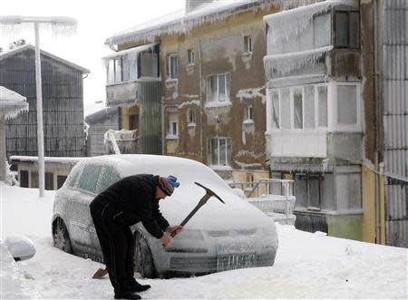 A man smashes ice with a pickaxe next to car covered with ice in Postojna February 3, 2014. REUTERS/Srdjan Zivulovic