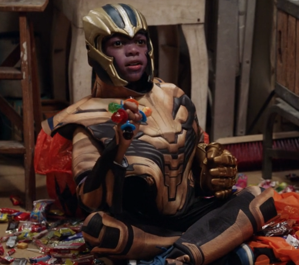 Baby Thanos sitting on the ground surrounded by candy and ring pops on his fingers