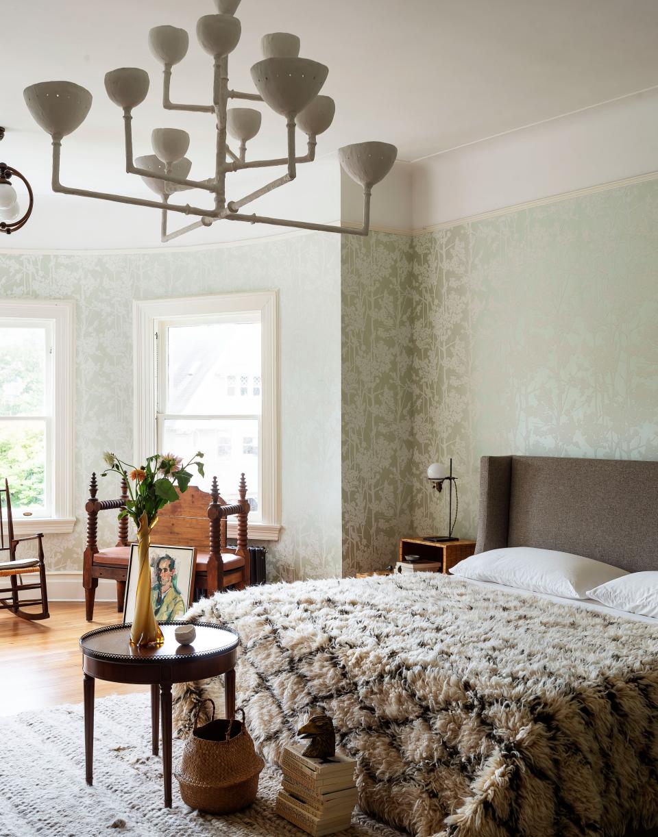 In the primary bedroom, a wallcovering in a subdued shade of green continues the bucolic mood. The chandelier is by Stephen Antonson.