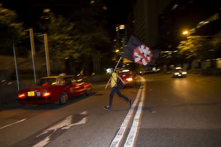 A pro-democracy activist carrying a flag against China's Communist Party runs across a road outside the hotel where China's National People's Congress (NPC) Standing Committee Deputy General Secretary Li Fei is staying, in Hong Kong September 1, 2014. REUTERS/Tyrone Siu