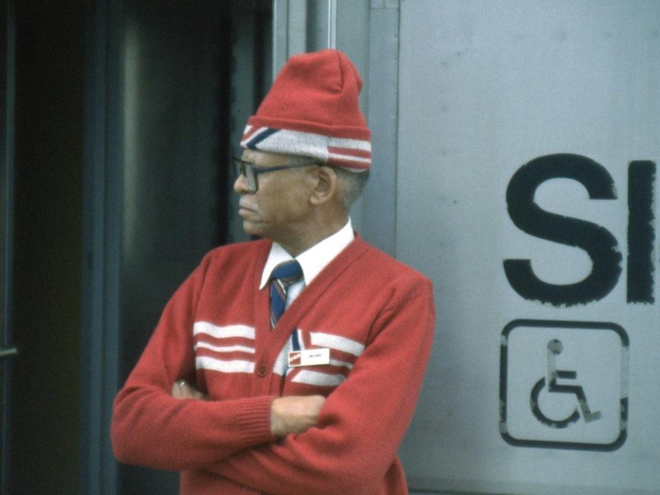 man in red amtrak uniform with beanie and white stripes, arms folded