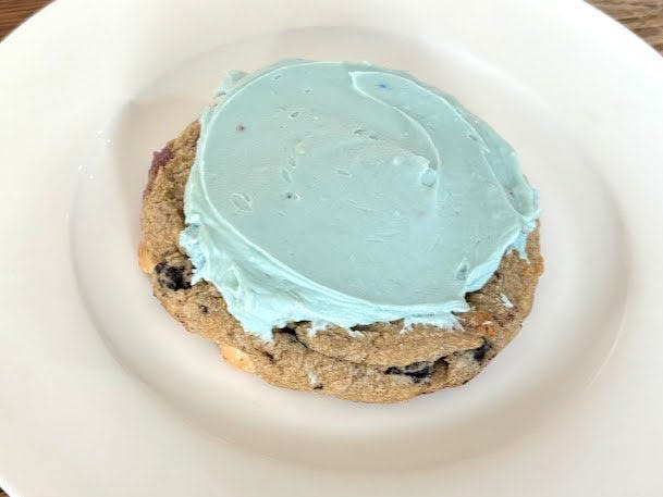 A cookies-and-cream cookie topped with blueish-green frosting on a white plate.