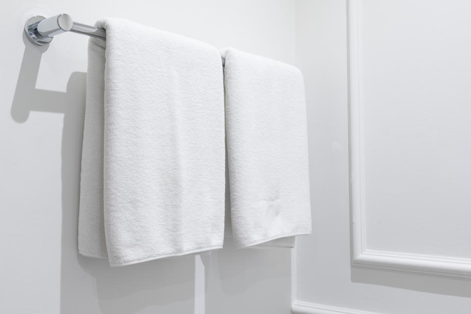 Two white towels hang neatly next to each other on a silver towel rack in a minimalist bathroom